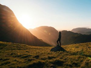 Serene mountain landscape with a woman standing on a rock during sunset, symbolizing personal growth and life coaching.
