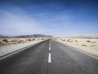 Alt text: Long empty desert highway stretching towards distant mountains under clear blue sky.
