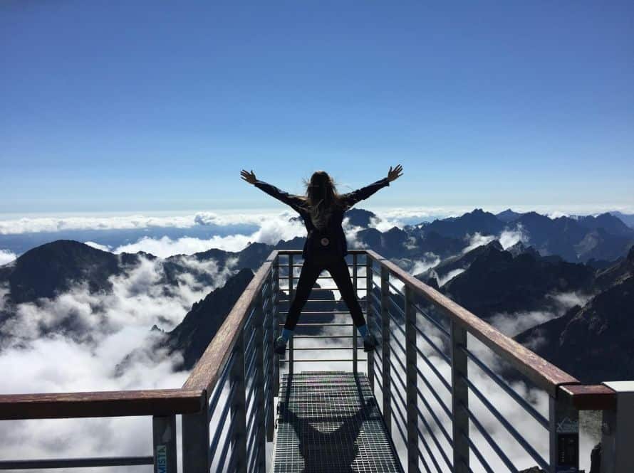 person standing on mountain platform with arms raised above clouds Person standing on a mountain platform with arms raised above the clouds, symbolizing becoming unstuck with goals