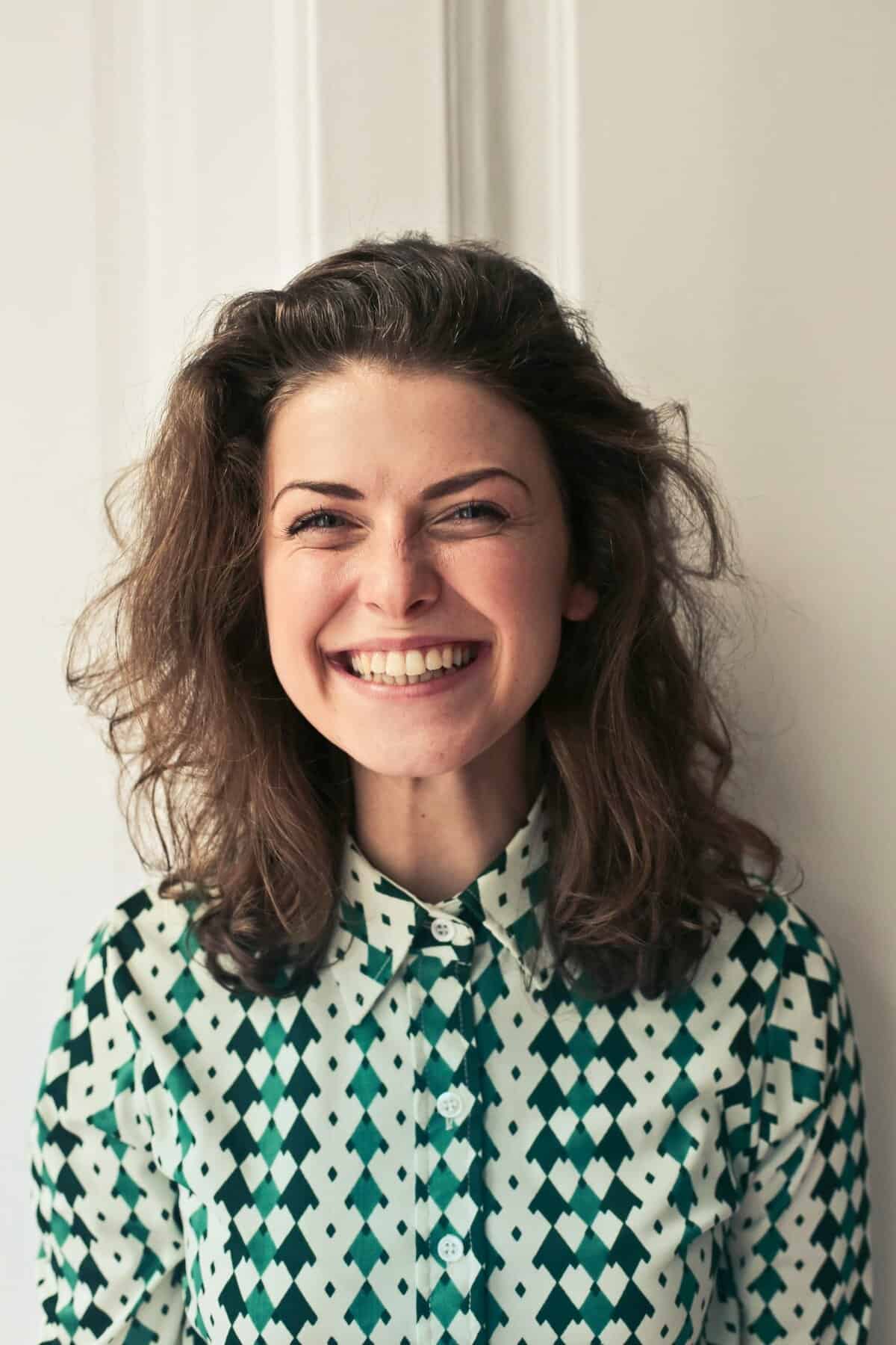 Smiling woman with curly hair wearing a patterned shirt standing indoors
