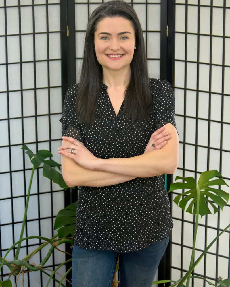 Life coach standing indoors with arms crossed, smiling confidently in a calm, welcoming space