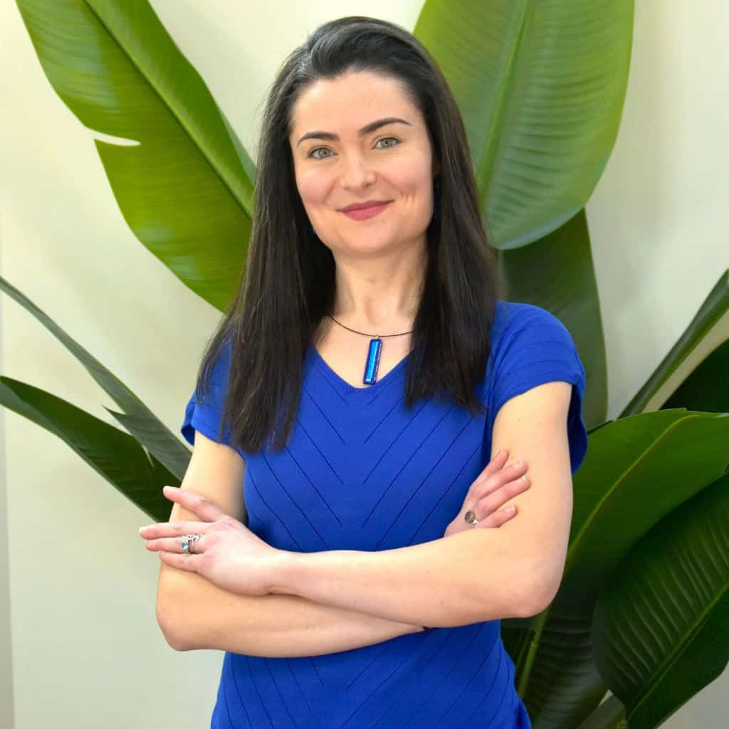 Life coach standing indoors with arms crossed, smiling confidently in a calm, welcoming space